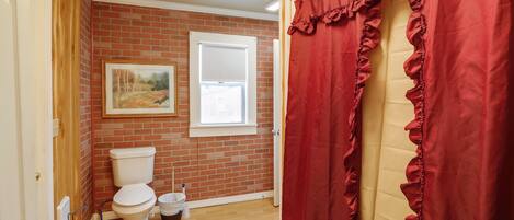 A bathroom with a toilet, a window, and a red curtain.