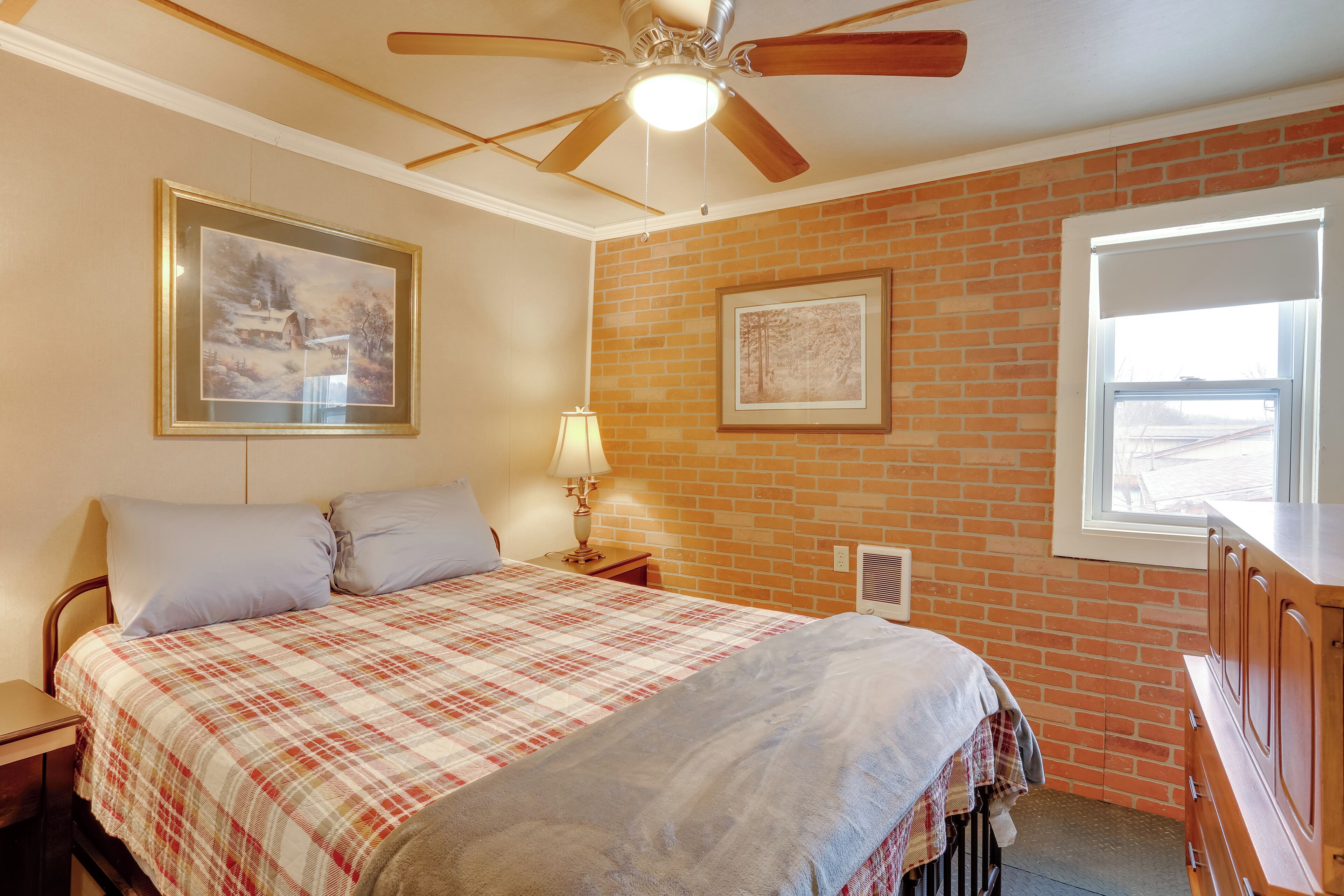 A bedroom with a bed, a ceiling fan, a window, and a brick wall.