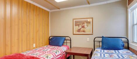 Ein Zimmer mit zwei Betten, jeweils mit einer Steppdecke, einem kleinen Tisch und einem Bild an der Wand.
