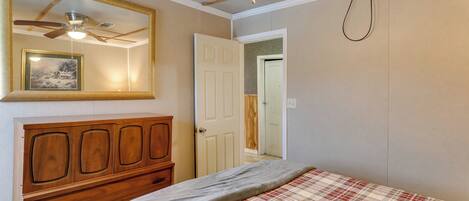 Un dormitorio con cabecera de madera, ventilador de techo, cama con colcha escocesa y una puerta que da a otra habitación.