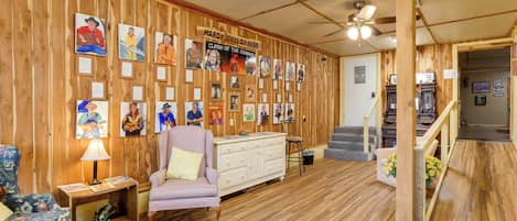 A room with wooden walls, a ceiling fan, a staircase, and a wall of framed pictures.