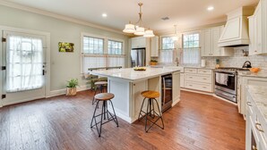 A spacious kitchen with a large island, wooden flooring, white cabinetry, and stainless steel appliances. - Historical 1835 Home in Grand Coteau! (Sunset)