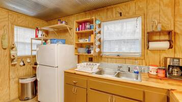 A compact kitchen with wooden cabinets, a sink, a refrigerator, and a window with blinds.