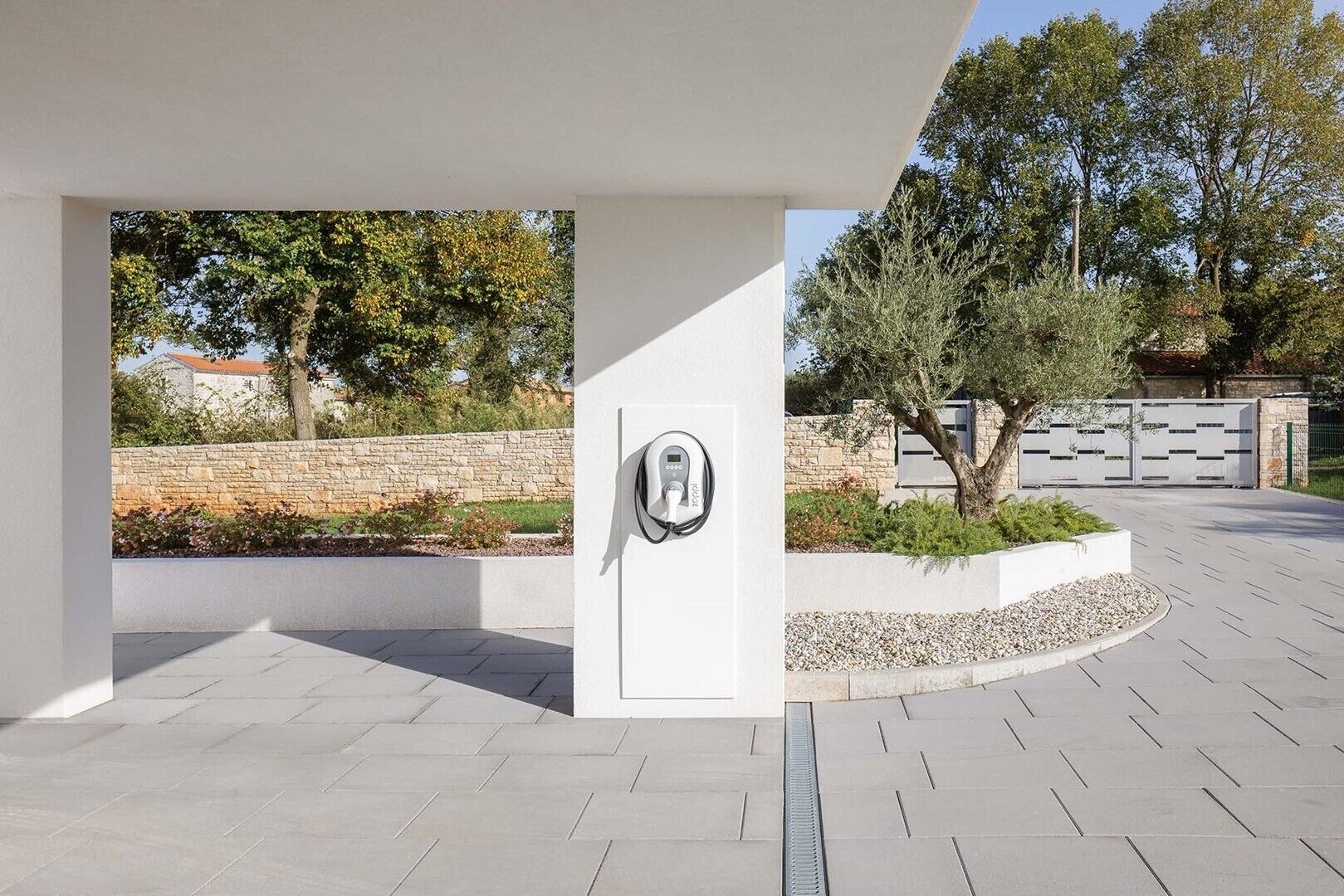 A modern building with a clean, minimalist design, featuring a stone wall and a landscaped area with a tree and shrubs.