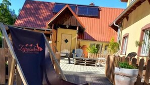 A patio area with a folding chair, a wooden fence, and a building with a red roof. - Apartament Harmont Montis (Szklarska Poreba)