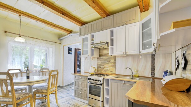 A kitchen with wooden cabinets, a gas stove, and a dining area with chairs and a table. - Apartament Harmont Montis (Szklarska Poreba)