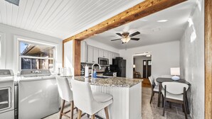 A modern kitchen with a central island, bar stools, and a dining area with a table and chairs. - 3BR/3BA 1940s Bungalow Near Expo Square. Pet friendly! (Tulsa)