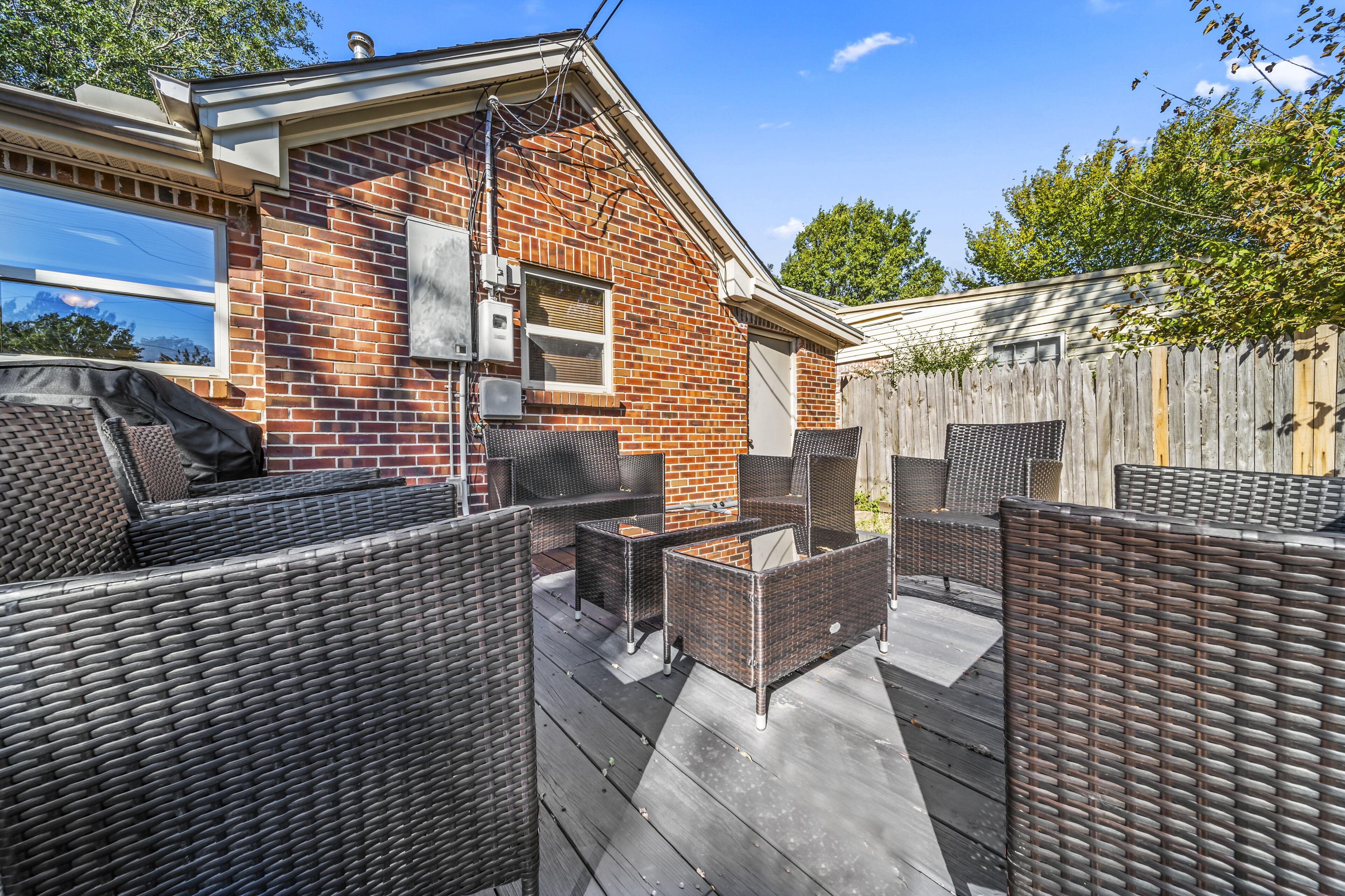 A patio area with wicker furniture and a brick building in the background.