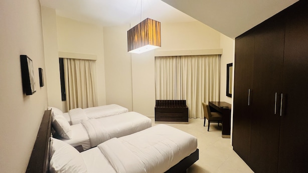 A hotel room with two beds, a desk, a wardrobe, and a hanging light fixture. - AlRaef Luxury Apartments (Dubai)