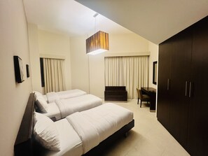 A hotel room with two beds, a desk, a wardrobe, and a hanging light fixture. - AlRaef Luxury Apartments (Dubai)