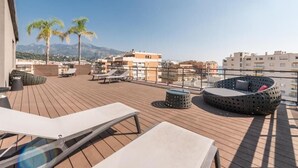 Una terraza en la azotea con sillones, un espacio de descanso circular y palmeras.