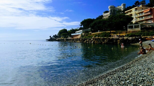 Un hotel frente al mar con costa rocosa, cielo azul despejado y mar tranquilo.