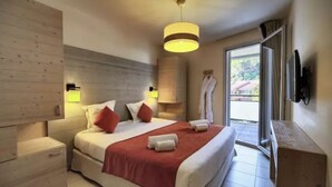 Una habitación de hotel moderna con una cama grande, una mesita de noche, una televisión montada en la pared y una puerta de cristal corredera que da a un balcón.