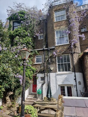 A traditional brick building with multiple windows, a red door, and purple flowering vines.
