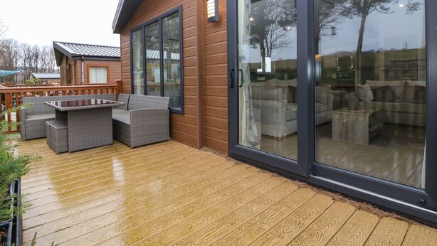 A wooden deck with outdoor furniture, a sliding glass door, and a view of the surrounding area.