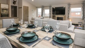A modern living room with a dining area set for six, a flat-screen TV, and a fireplace.