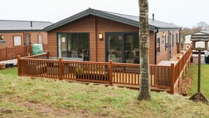 A wooden cabin with a deck, large sliding glass doors, and a covered outdoor seating area.