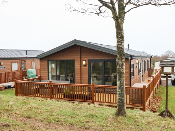 A wooden cabin with a deck, large sliding glass doors, and a covered outdoor seating area.