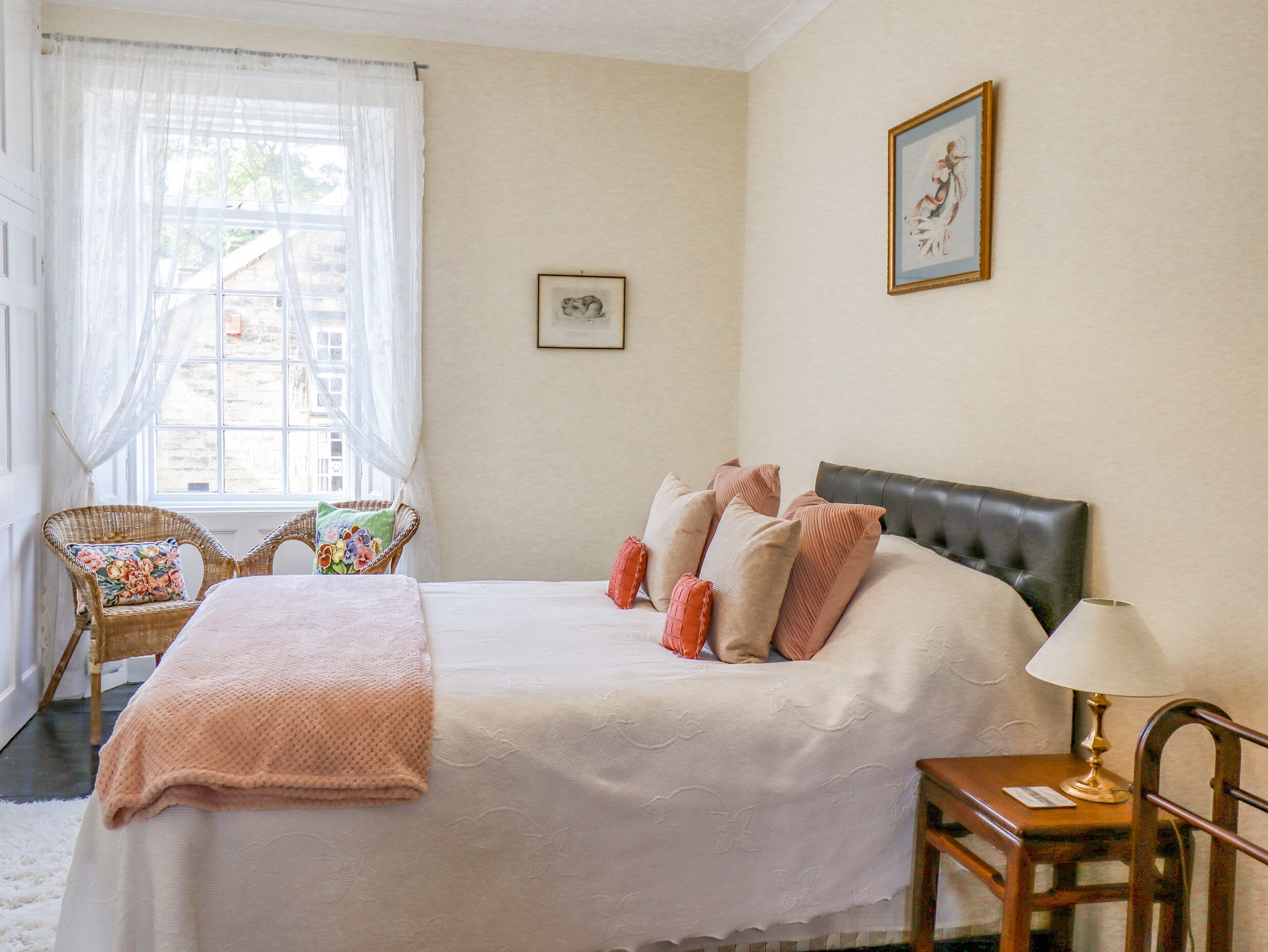 Une chambre bien rangée, avec un lit, une chaise, une lampe et une fenêtre avec des rideaux.