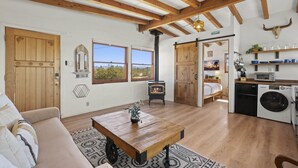 Een gezellige woonkamer met een houten tafel, een bank en een open haard. Er is een keukenhoek met een wasmachine en een magnetron.