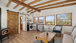 Een rustiek interieur met een houten plafond, een keuken met een wasmachine, een eethoek met een tafel en een groot raam met uitzicht.