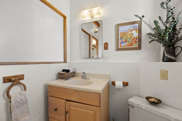 A bathroom with a wooden vanity, a sink, a mirror, a toilet, and a framed artwork on the wall.