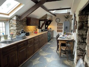 A kitchen with a stone wall, wooden cabinets, a dining table with chairs, and a clock on the wall.