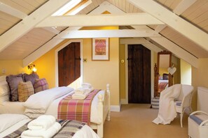 A cozy attic bedroom with a sloped ceiling, a bed with multiple pillows, a chair, and a mirror.