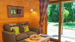 A cozy cabin interior with a wooden couch, a small table, and a window with a view of greenery. - Fiddlers Green Log Cabin, Tenby (Saint Florence)
