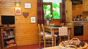 A cozy cabin interior with a wooden interior, a dining table with chairs, a television, and a kitchen area. - Fiddlers Green Log Cabin, Tenby (Saint Florence)