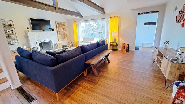A modern living room with a large blue sectional sofa, a wooden bench, a flat-screen TV, and a fireplace. - Heated pool hot tub play set screened porch sauna putting green (Harbert)