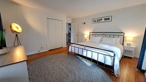 A bedroom with a bed, bedside lamps, a sign reading "SLEEP INN", and a plant.