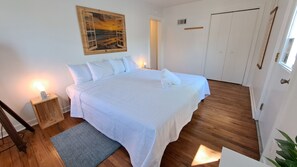A neatly made bed with white bedding, a wooden floor, a small bedside table with a lamp, and a painting on the wall. - Heated pool hot tub play set screened porch sauna putting green (Harbert)