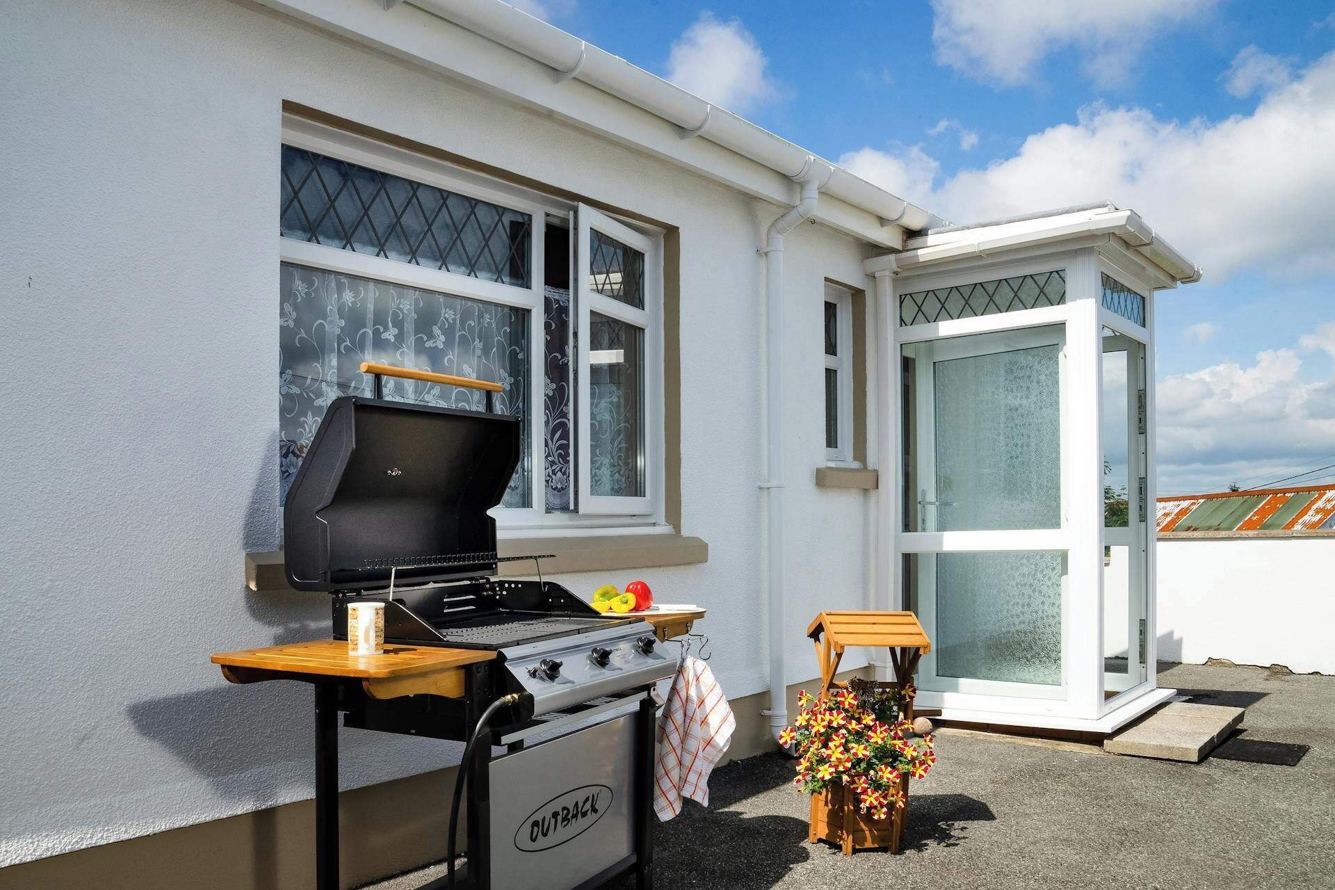 Een barbecue, een kleine tafel en een bloemstuk buiten een huis.