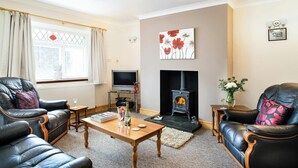 A living room with a fireplace, leather sofas, a television, and a window with curtains. - 2 Rock Cottage, Llansteffan (Llansteffan)