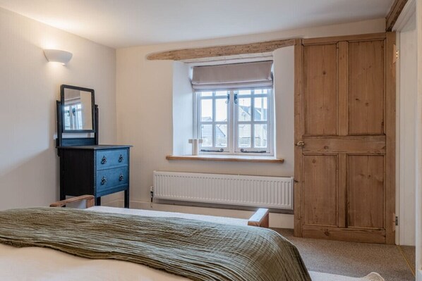 A bedroom with a bed, a dresser, a window with a view, a radiator, and a wooden door.