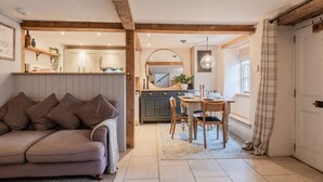 A cozy living room with a sofa, a dining area with a table and chairs, and a kitchen in the background. - The Gamekeeper`s Cottage - Stunning 2 Bed (Leafield)
