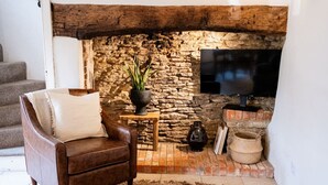 A cozy living room with a stone fireplace, a leather armchair, a television, and rustic decor. - The Gamekeeper`s Cottage - Stunning 2 Bed (Leafield)