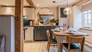 A kitchen with a dining table set for four, wooden chairs, a large mirror, and a hanging light fixture. - The Gamekeeper`s Cottage - Stunning 2 Bed (Leafield)