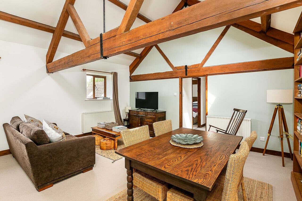 A dining area with a wooden table, wicker chairs, a sofa, and a television in the background.