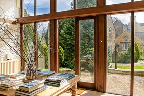 A room with a large window, a wooden table with books, and a vase with branches. - Stunning Barn Conversion - Peaceful Retreat (Old Chalford)