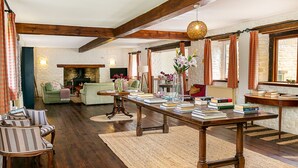 A cozy living room with a fireplace, wooden beams, a long table with books, and a green sofa. - Stunning Barn Conversion - Peaceful Retreat (Old Chalford)