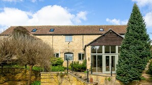 A stone building with a tiled roof, a glass entrance, and a well-maintained garden with a large evergreen tree. - Stunning Barn Conversion - Peaceful Retreat (Old Chalford)