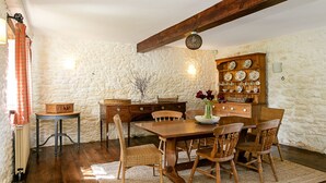 A rustic dining room with a wooden table, wicker chairs, and a stone wall. - Stunning Barn Conversion - Peaceful Retreat (Old Chalford)