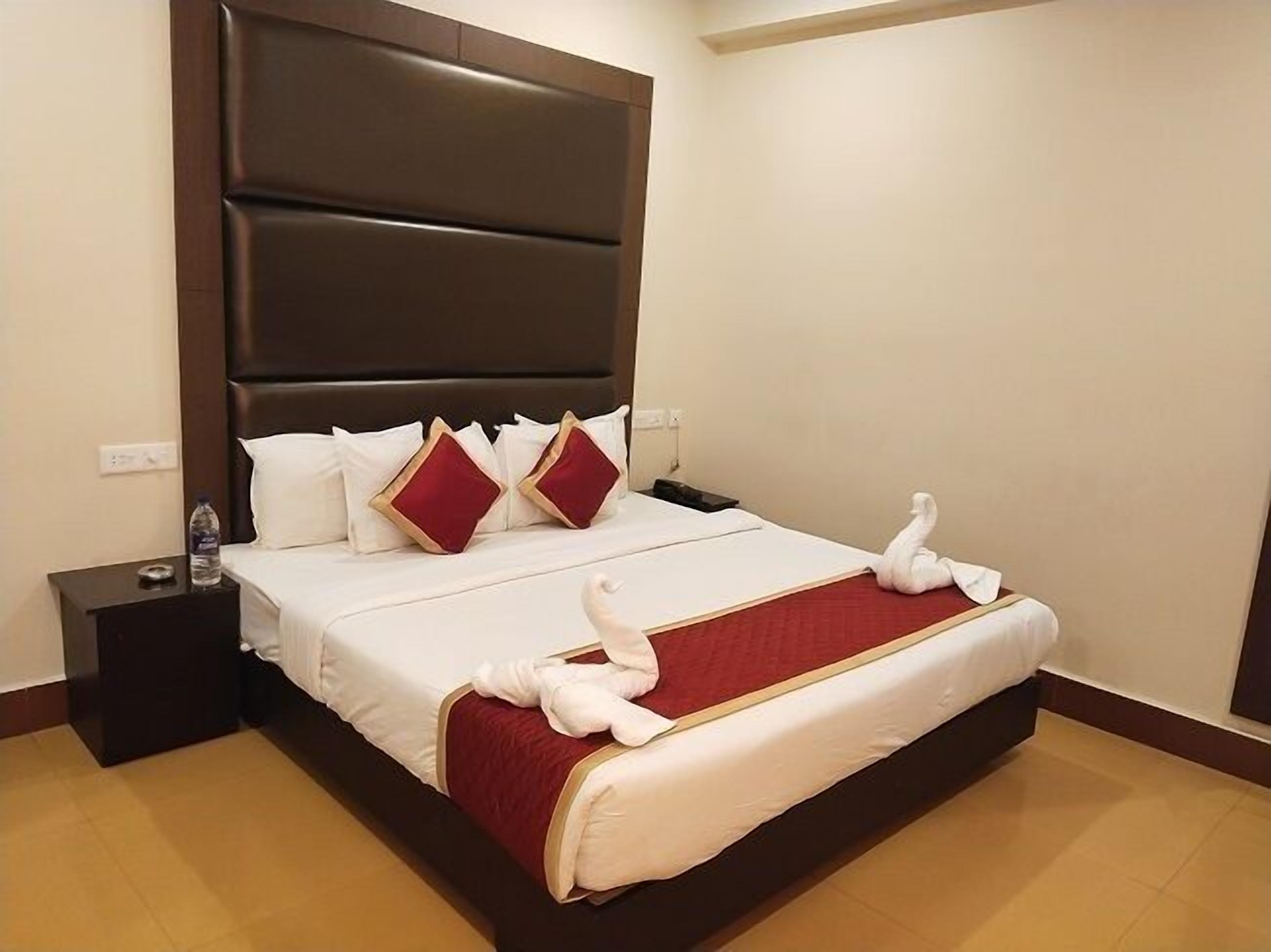 Een hotelkamer met een groot bed, een donker hoofdeinde, witte en rode kussens, een rode spreideken en een zwanendecoratie.