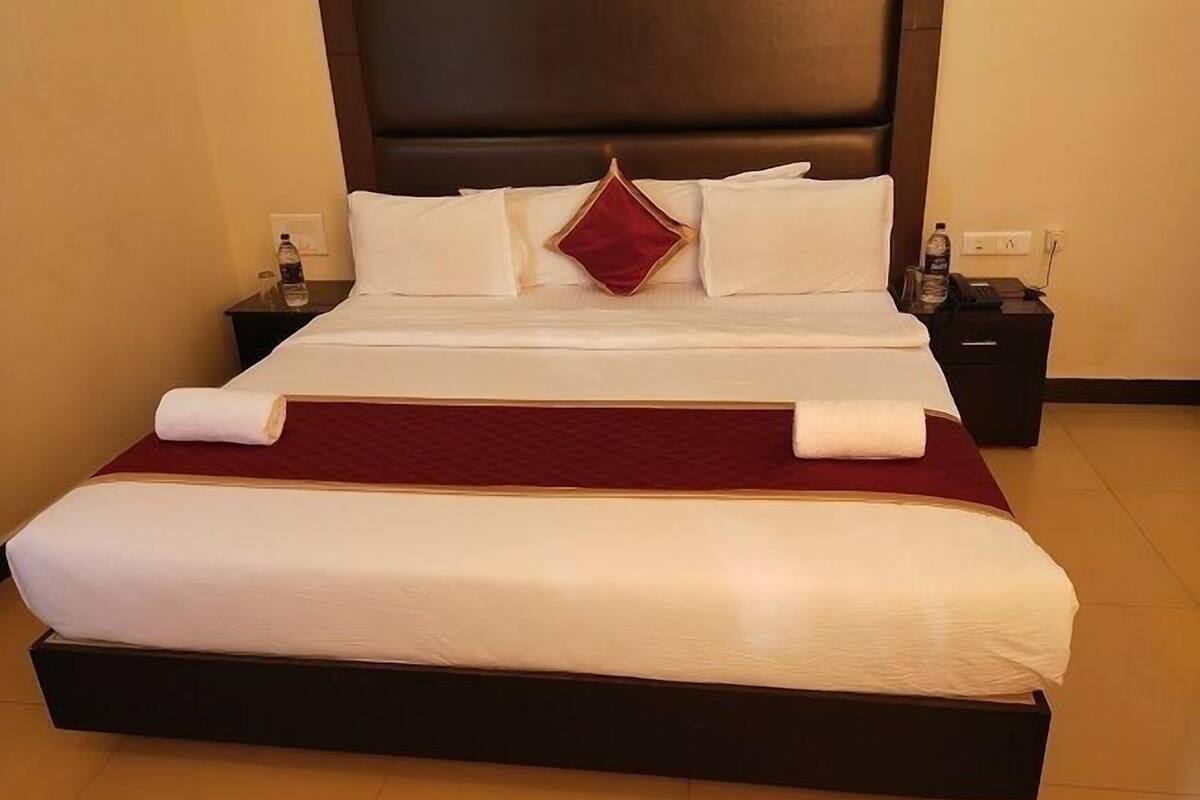 A neatly made bed with white linens, a red throw blanket, and a matching pillow.