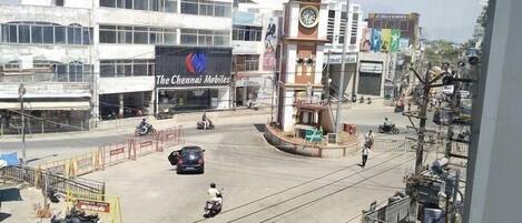 Una calle urbana concurrida con una glorieta, una torre del reloj y un edificio que dice "The Chennai Mobiles".