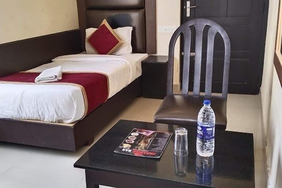 A hotel room with a bed, a chair, a small table with a magazine, a bottle of water, and a door.