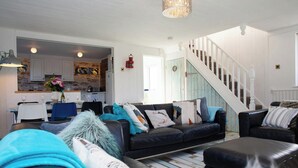 Un salon avec un canapé en cuir noir, un coin repas avec une table bleue et un escalier avec des rampes blanches.