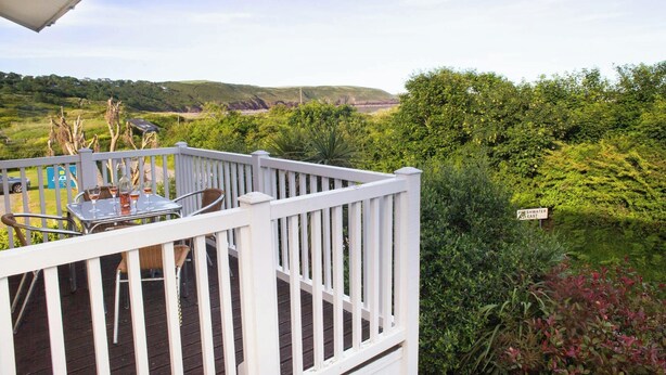 Un balcon avec une table et des chaises, donnant sur un paysage verdoyant avec des collines et un panneau indiquant « Freshwater East ».